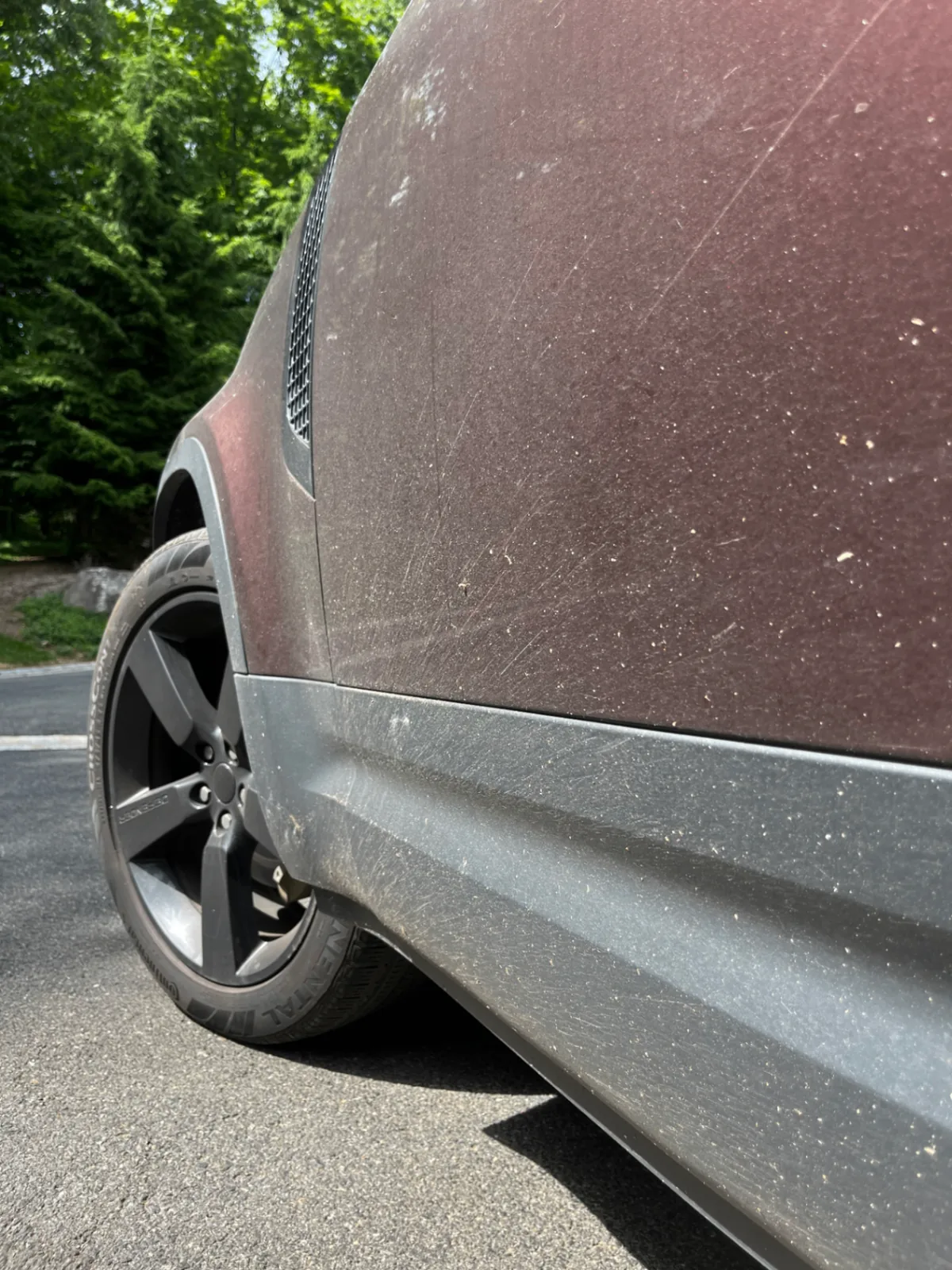 Side of a maroon SUV covered in road dust before Bluefin detailing